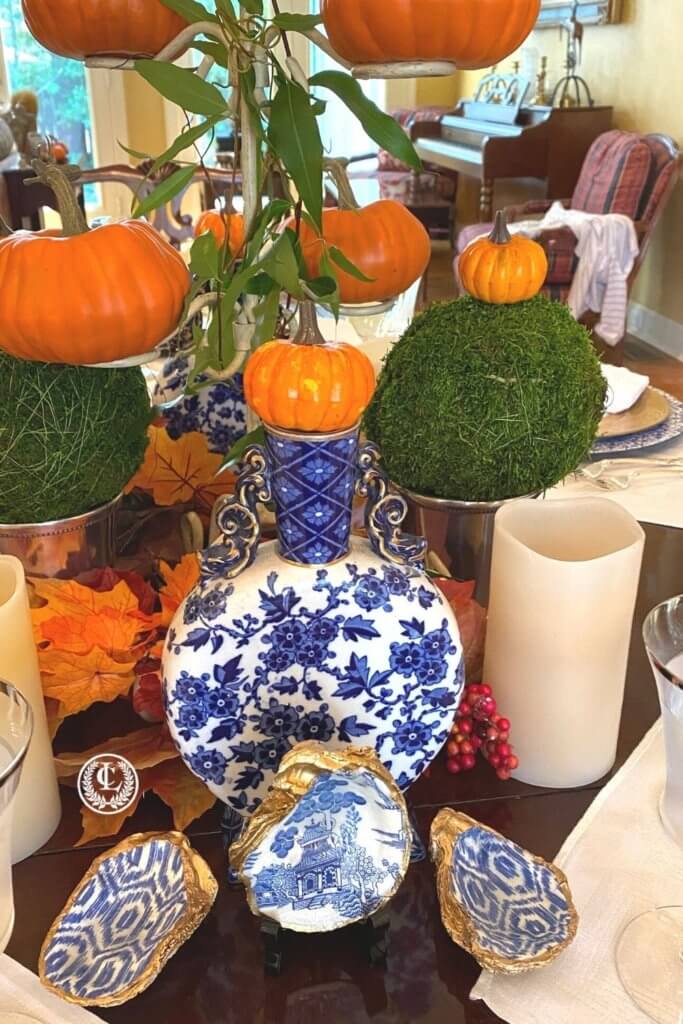 Blue and white decor with orange pumpkins makes an inviting Thanksgiving centerpiece.   The oyster shell dishes embellish the centerpiece as well.
